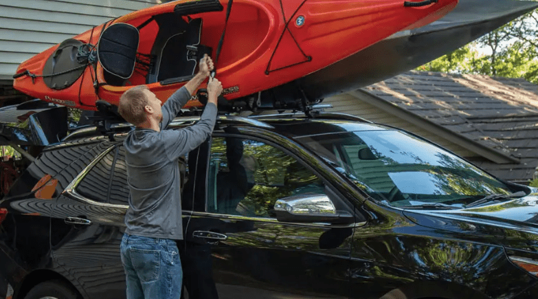 A man is holding onto the roof of his car